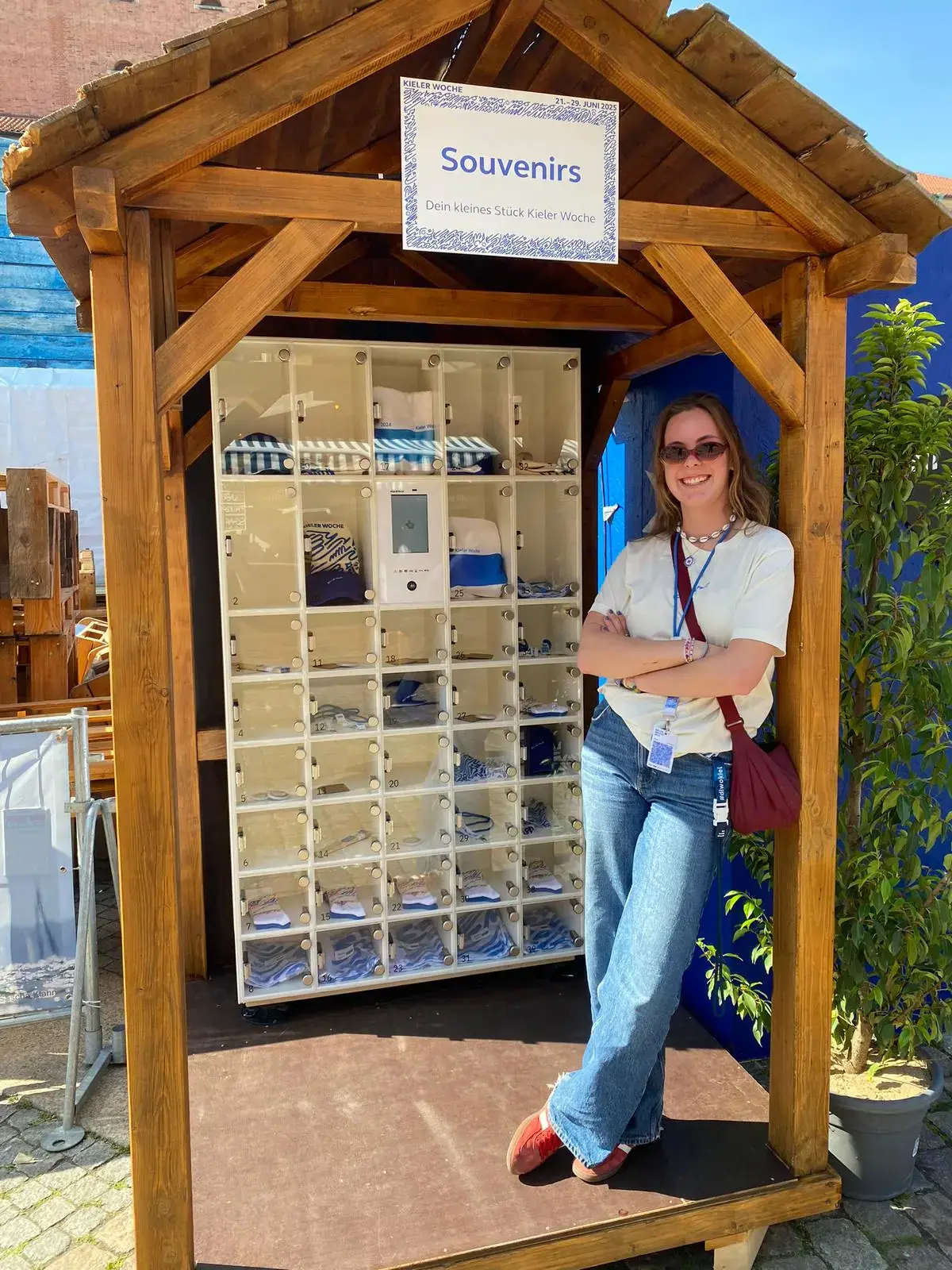 Lächelnde Frau neben einer marktbox in einer Holzhütte, die Souvenirs für die Kieler Woche anbietet