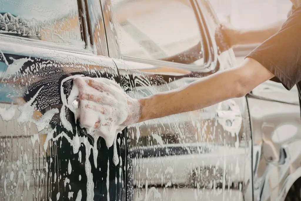 Hand wäscht ein dunkles Auto mit einem Schwamm und weißem Seifenschaum