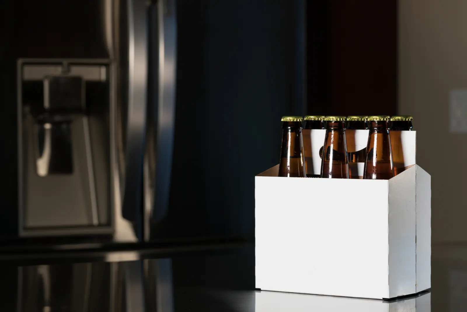 Sechs braune Bierflaschen in einem weißen Karton auf einer dunklen, glänzenden Oberfläche