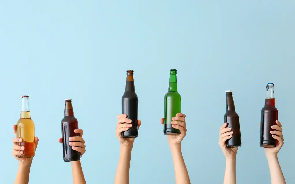 Sechs Hände halten verschiedene Bier- und Getränkeflaschen vor einem hellblauen Hintergrund hoch