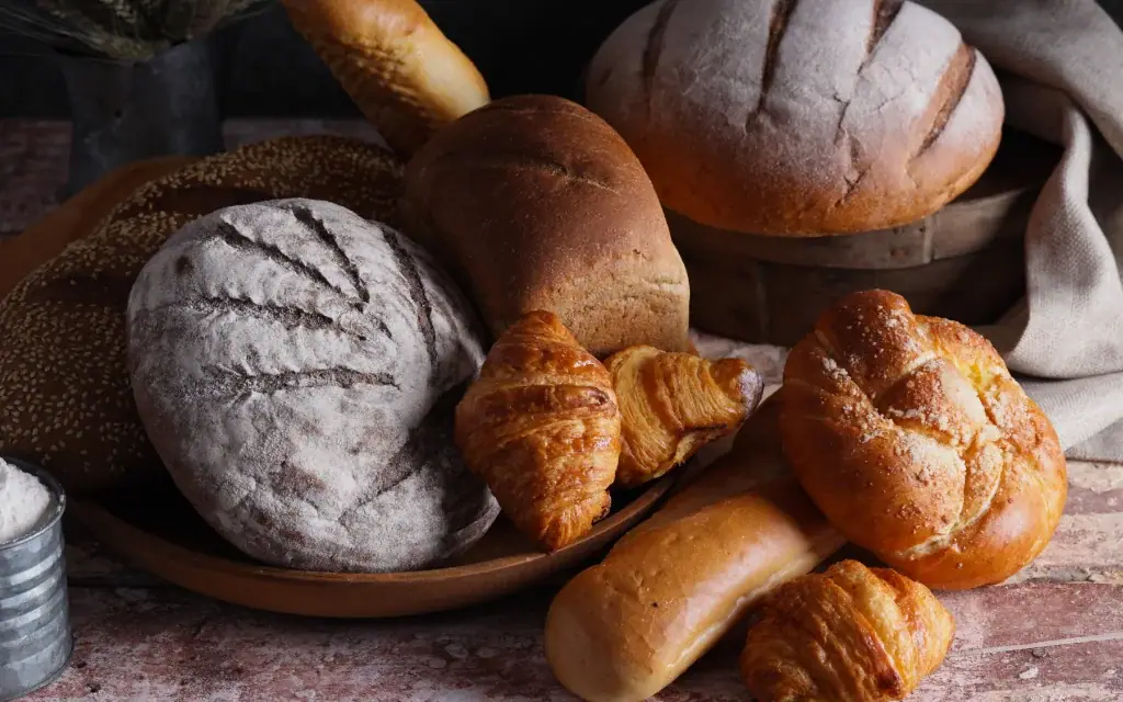 Verschiedene frische Brotsorten, Baguettes und goldbraune Croissants auf einer rustikalen Holzplatte angerichtet