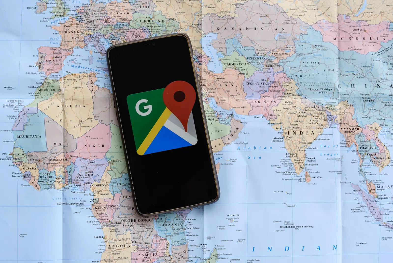 Smartphone mit dem Google Maps Logo auf dem Display auf einer Weltkarte aus Papier