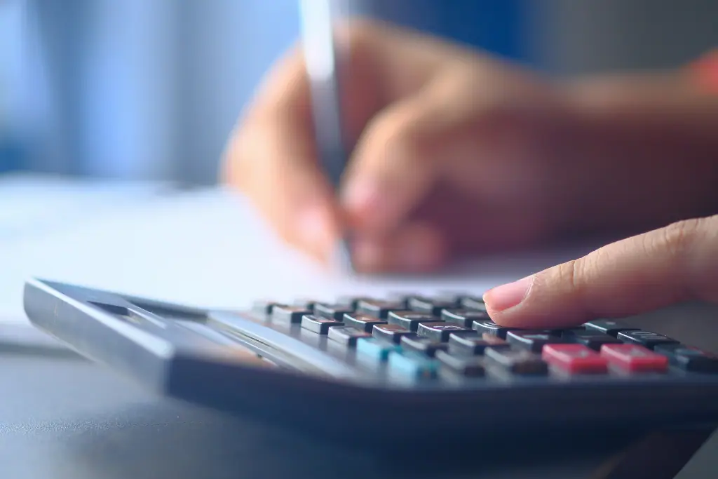 Eine Hand bedient einen Taschenrechner, während die andere Hand einen Stift über Papier hält