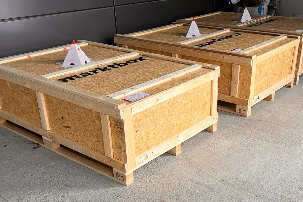 Drei große Holztransportkisten mit marktbox-Logo stehen versandbereit auf einem Betonboden
