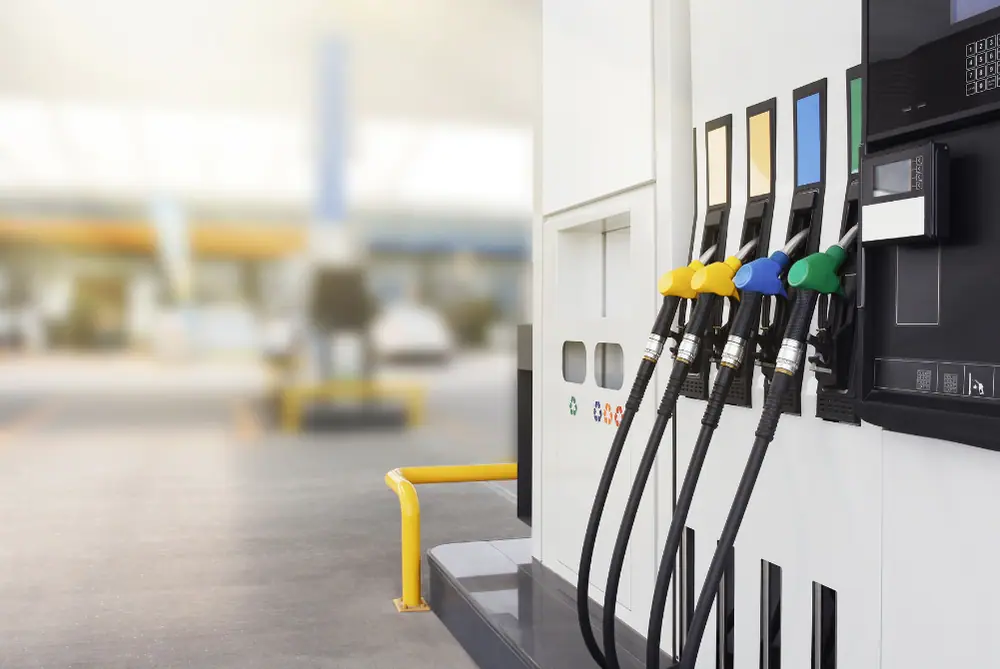 Zapfsäule mit vier farbigen Zapfpistolen vor dem unscharfen Hintergrund einer Tankstelle