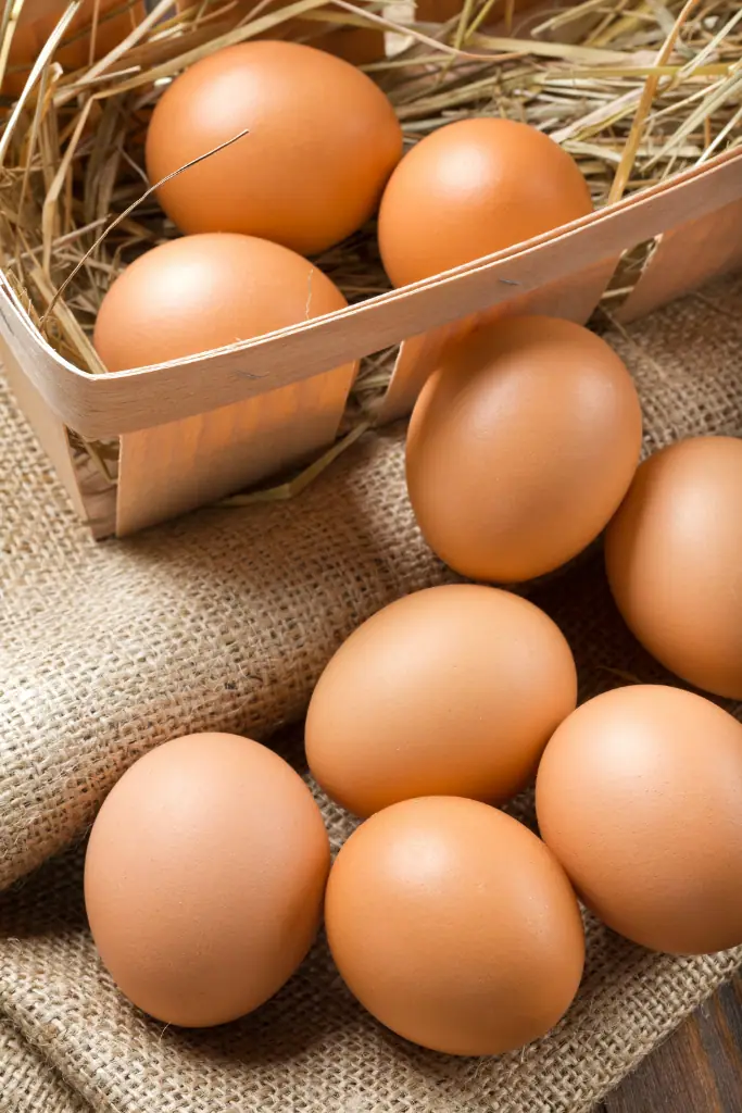 Braune Hühnereier in einem Holzkörbchen mit Stroh und auf grobem Sackleinen