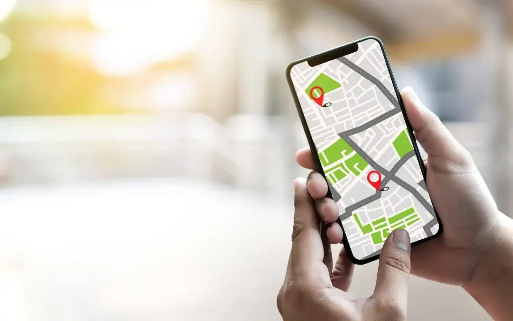 Hände halten ein Smartphone mit einer digitalen Karte und roten Standort-Pins vor hellem Hintergrund