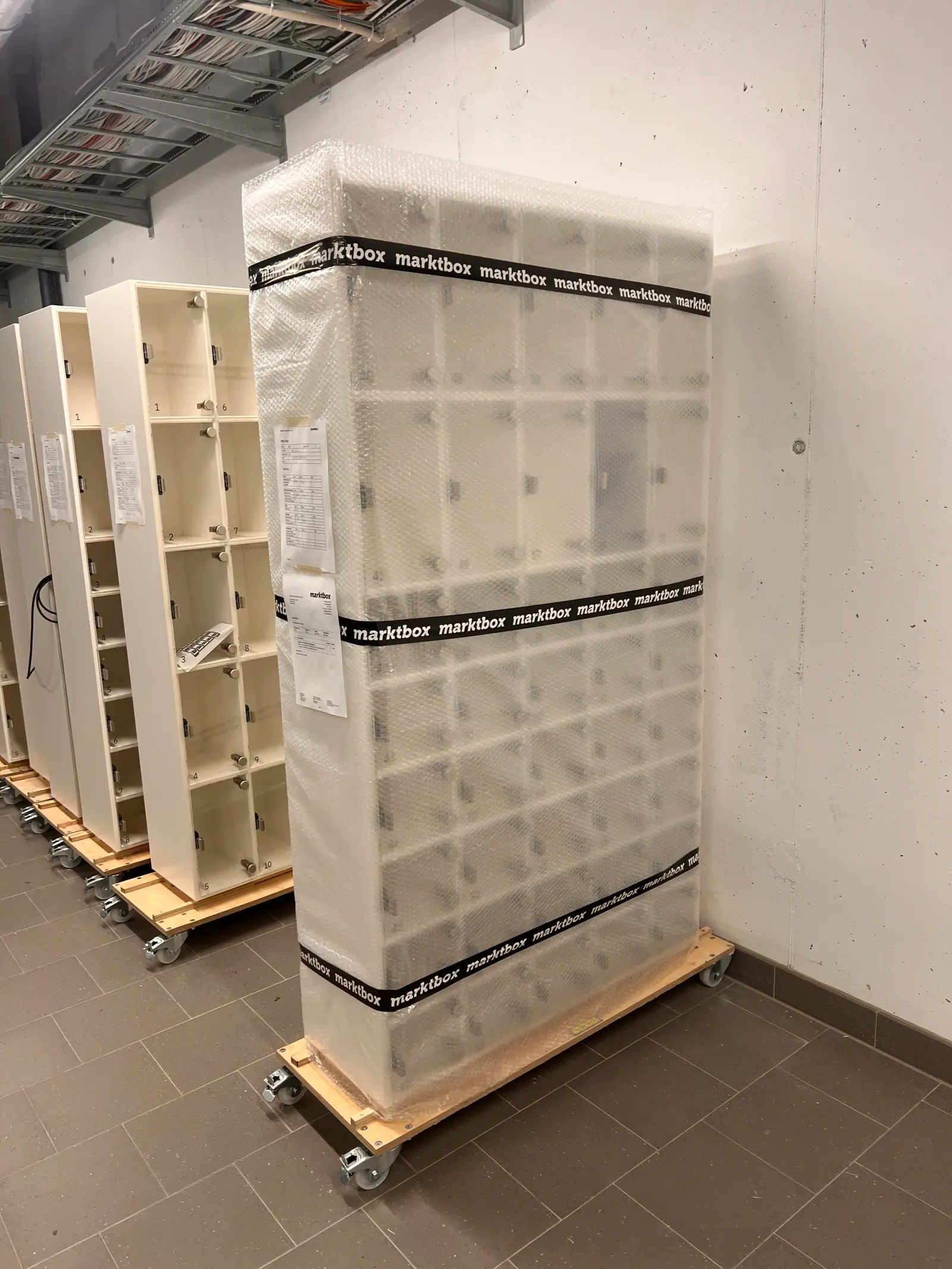 Mehrere weiße Marktboxen auf Rollwagen, die vorderste für den Versand in Luftpolsterfolie verpackt