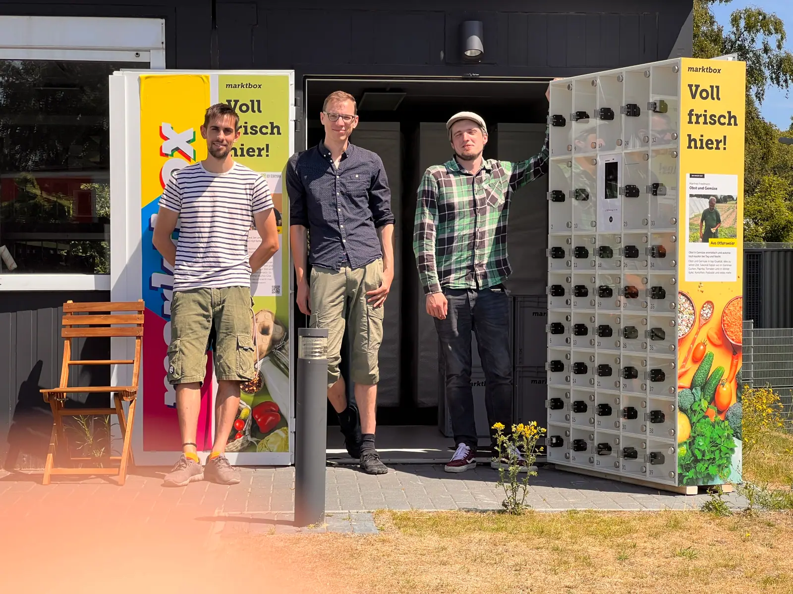 Drei Männer stehen vor einer marktbox-Abholstation mit zahlreichen Schließfächern im Freien