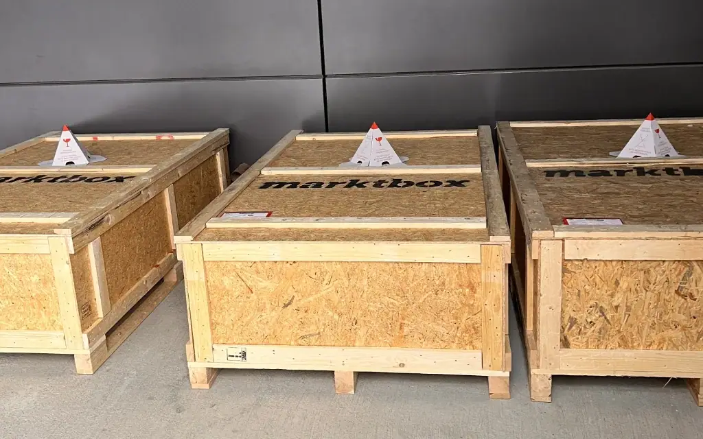 Drei große Holztransportkisten mit marktbox-Logo stehen nebeneinander für den Versand bereit